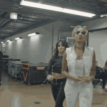 two women are dancing in a hallway with an exit sign on the wall behind them