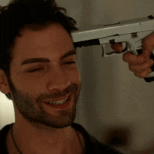 a man with a beard is smiling while holding a gun to his head