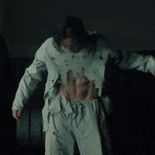 a man wearing a green shirt with holes in it is standing in a dark room