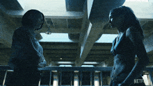 two women standing next to each other in a dark room with a netflix logo on the bottom right