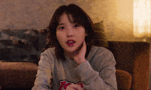 a woman sitting on a couch with her hand on her face wearing a grey sweatshirt with the letter r on it