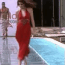 a woman in a red dress is walking down a runway next to a pool .