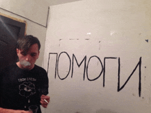 a man is smoking a cigarette in front of a wall that has the word pomogi written on it