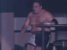 a man without a shirt is in a boxing ring with a referee in the background