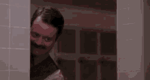 a man with a mustache is peeking out of a bathroom door .