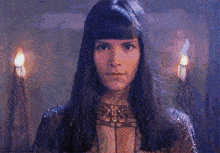 a woman with long black hair is standing in a dark room with candles behind her .