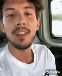 a man with a beard is sitting in the back seat of a car talking .