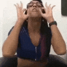 a woman wearing glasses and a blue shirt is making a funny face with her hands .