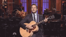 a man in a suit and tie plays an acoustic guitar on stage