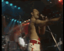 a man without a shirt is singing into a microphone on a stage in front of a crowd .