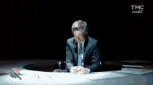 a man in a suit and tie is sitting at a table with tmc insight written on the bottom of the screen
