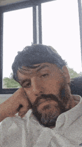 a man with a beard is sitting in front of a window with his hand on his face