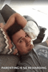 a man is laying on a couch with a baby on his head and the caption parenting is so rewarding .