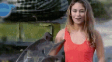 a woman in a red tank top is standing next to a dolphin .