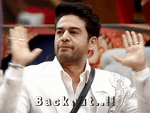a man in a white suit says backout !!! with his hands in the air