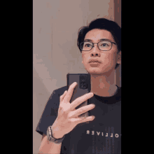 a man wearing glasses takes a selfie in front of a mirror with his phone