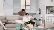 a man is sitting on a couch in a living room with a woman standing behind him .