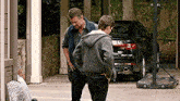 two men are standing next to each other in front of a car .