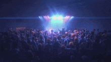 a crowd of people dancing in front of a stage with a blue light behind them