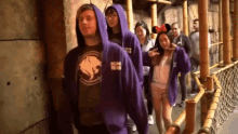 a group of people are walking down a hallway and one of them is wearing a hoodie with a lion on it