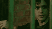 a man is behind a green fence and looking out .