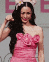a woman in a pink dress with flowers on the top is standing on a stage .
