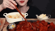 a woman is eating food with chopsticks and a bowl of food in the background
