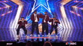 a group of men are performing on a stage with a nbc logo in the background