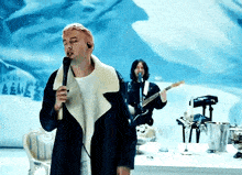 a man singing into a microphone while another man plays guitar