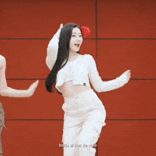 a woman in a white crop top and white pants is dancing in front of a red wall ..