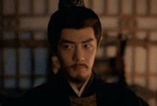 a man with a beard and a crown on his head looks at the camera .