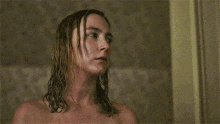 a naked woman with wet hair is standing in front of a wall looking up .