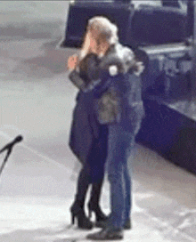 a man and a woman hugging on a stage with a microphone behind them