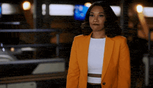 a woman in a yellow jacket and white crop top is standing in front of a building .