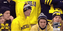 a group of people wearing michigan sweatshirts are sitting in a stadium