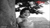 a woman is leaning against a tree with her hand on her face .