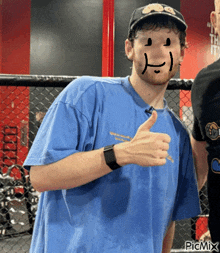 a man in a blue shirt with a smiley face drawn on his face is giving a thumbs up