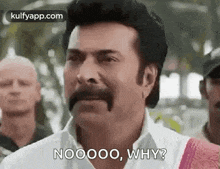 a man with a mustache is standing in front of a crowd and asking why .