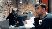 two men are sitting at a table with laptops in front of them and the words devoteam are on the screen