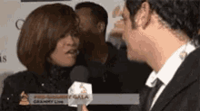 a man is talking to a woman in front of a sign that says pre-grammy gala