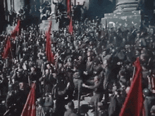 a large group of people holding red flags are standing in front of a building .