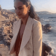 a woman in a striped jacket is standing on a rocky beach near the ocean