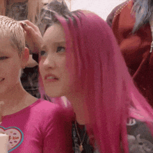 a girl with pink hair is getting her hair done by a woman .