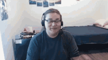 a man wearing headphones and glasses is sitting in a bedroom .