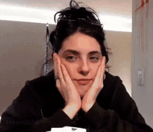 a woman with glasses and a nose ring is sitting with her hands on her face .