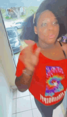 a woman is standing in front of a window wearing a red tie dye shirt .
