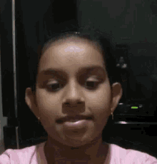 a young girl in a pink shirt is making a funny face and looking at the camera .