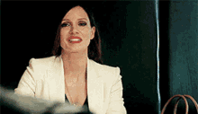 a woman wearing a white jacket and red lipstick is smiling while sitting at a table .