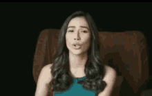 a woman in a blue dress is sitting in a chair making a funny face .