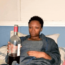 a woman is holding a bottle of wine while sitting on a bed .